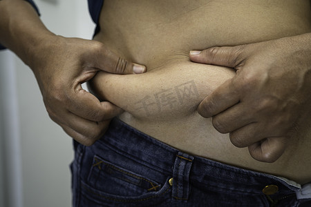 超重的亚洲女性展示并用手挤压肥胖的腹部。