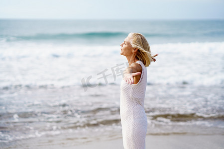 成熟的女人在沙滩上张开双臂，度过闲暇时光，享受闲暇时光