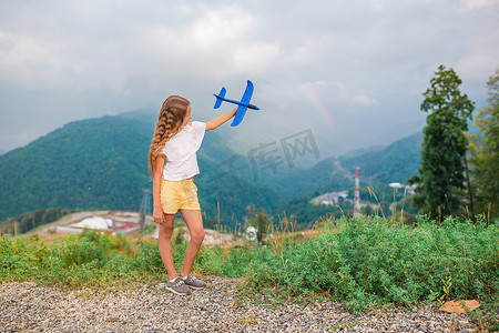 纸飞机花纹摄影照片_快乐的小女孩手里拿着玩具飞机在山上