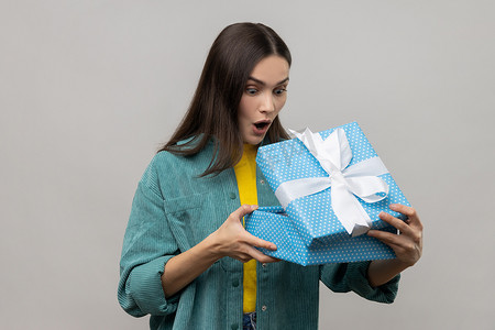 惊讶的黑发女人打开蓝色礼盒，用惊奇的表情看着里面
