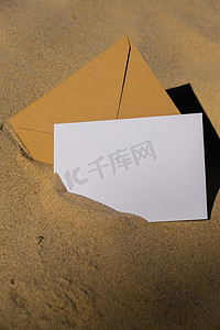 米色自然色调的信封，上面有空白的白纸便条复制空间，供您在沙滩上的文字中使用。