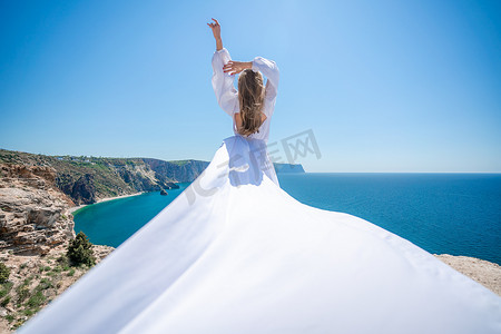 金发碧眼的长发在阳光明媚的海边穿着白色飘逸的连衣裙，后视，丝绸面料在风中飘扬。