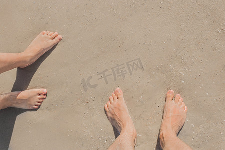 一个男人和一个女孩的腿站在海边潮湿的沙滩上，俯视