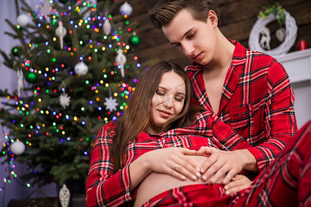 孕晚期摄影照片_坐在女人身后的男人抱着她怀孕的肚子。