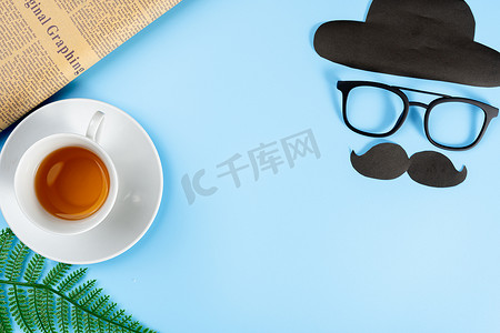 父亲节快乐背景概念，带眼镜、黑胡子、帽子、报纸、叶子和蓝色背景的茶杯，带有文本复制空间。