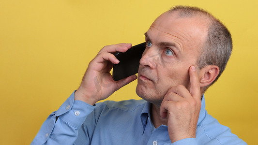 45-55 岁的英俊男子身穿蓝色衬衫，手里拿着智能手机。