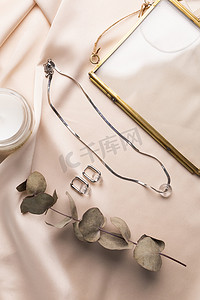 蓝珀项链摄影照片_丝绸背景上的极简主义几何银项链和圆形耳环。