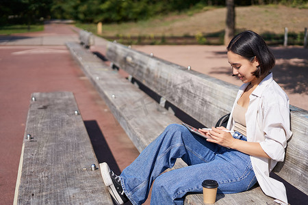 年轻的亚洲创意女孩用笔在平板电脑上画画，坐在公园的户外，画画