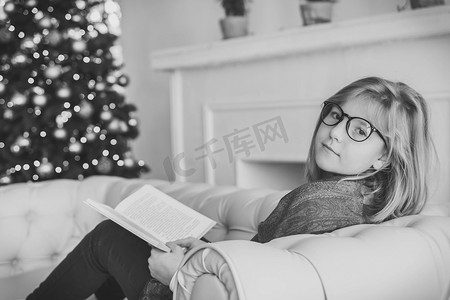 在圣诞树附近的沙发上看书的漂亮女孩