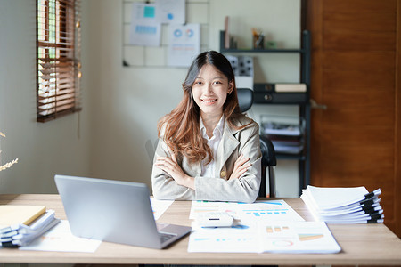 企业财务摄影照片_一位女企业主的画像，她在工作中使用电脑和财务预算文件成功地投资了她的企业时，脸上挂着快乐的笑脸
