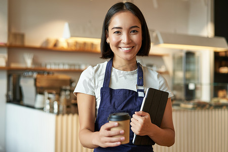 微笑的咖啡师，咖啡厅女服务员发出外卖咖啡订单，准备外卖卡布奇诺，站在蓝色围裙和平板电脑