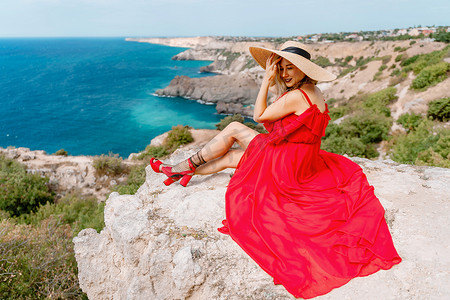 一位身着红色丝绸连衣裙的女子坐在海边，背靠群山，她的裙子在风中摇曳。