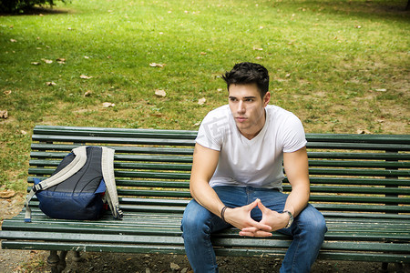 有精力的学生摄影照片_严肃地坐在公园长椅上的年轻男学生
