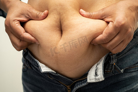 肥胖女性摄影照片_超重的亚洲女性展示并用手挤压肥胖的腹部。