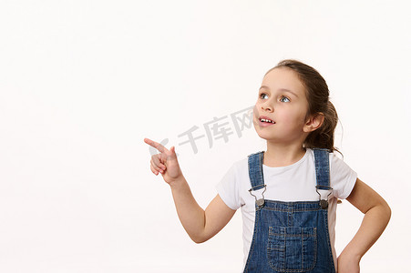 可爱的小孩，穿着蓝色牛仔服的可爱小女孩，用手指指着白色背景中的复制广告空间