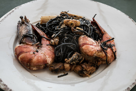 鱿鱼墨汁意大利面（黑色意大利面）配河虾或虾、贻贝和竹笋，放在白色陶瓷盘上。