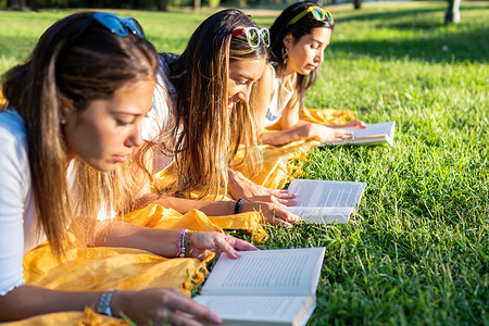 大学女学生早上躺在公园的草地上阅读一本平装书-在户外放松分享您的激情-回归旧的健康习惯-热爱大自然