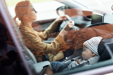 母亲专注于驾驶家庭汽车跑腿，而她的孩子则睡在她附近的婴儿汽车座椅上。