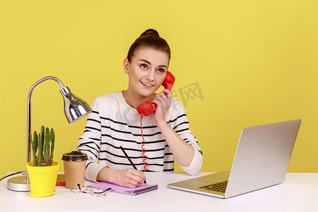 红色手写字摄影照片_在红色复古手机上聊天的女人有梦幻般的表情，坐在工作场所，用记事本写字