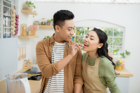 互相喂食摄影照片_美丽幸福的亚洲夫妇在厨房里互相喂食。