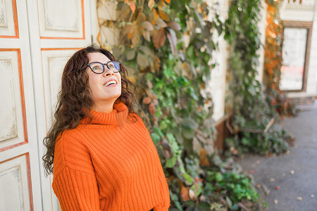 戴着时尚眼镜、身穿时尚橙色针织毛衣的迷人年轻女子的快乐肖像，背景是叶子复制空间和文本空白空间。