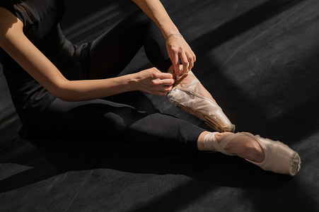 不露面的芭蕾舞演员坐在地板上，穿上足尖鞋。