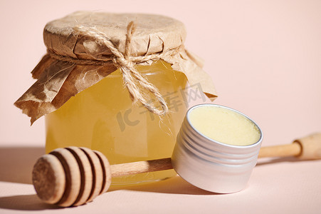 蜜蜡摄影照片_在米色柔和背景下，有选择地关注一个带蜡的罐子和一个装有有机蜂蜜的罐头。