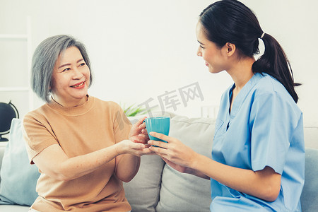 心满意足摄影照片_女性护理员为她心满意足的老年患者端上一杯咖啡。