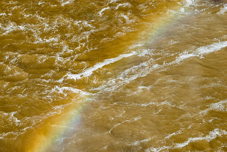 生动的彩虹横跨翻腾的泥泞河流