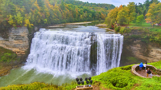 河流中巨大的汹涌瀑布穿过峡谷，树叶五颜六色，游客从远景欣赏