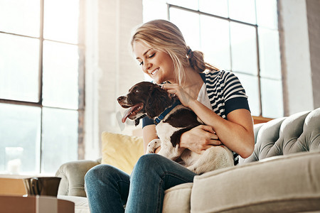 爱护狗摄影照片_客厅沙发上的女人、狗和平静的微笑，以在家中照顾动物、爱护和支持。