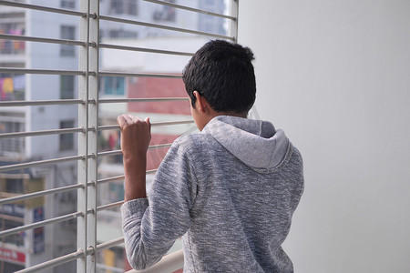 悲伤的十几岁男孩透过窗户看