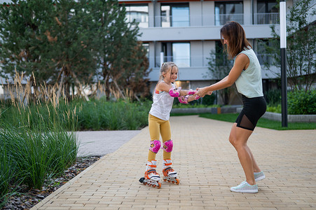 溜冰公园摄影照片_母亲帮助女儿学习溜冰。