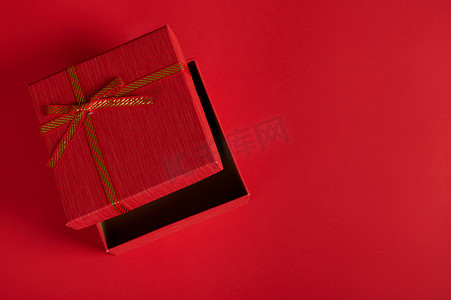 包装样机平铺图摄影照片_单色静物，带有一个打开的红色礼盒，红色背景上系着蝴蝶结，上面有复制广告空间。