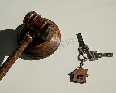 带有房子形状钥匙链的钥匙和白色背景上的法官槌。