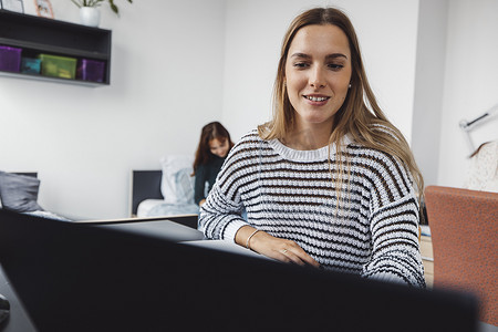 穿着条纹毛衣、微笑的白人女性在笔记本电脑上工作