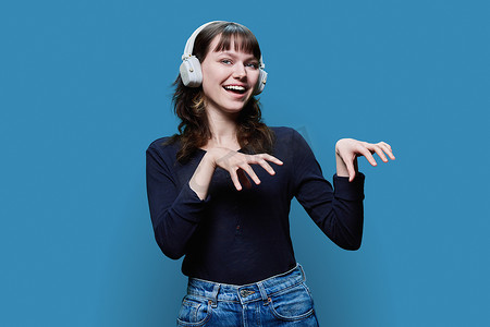 蓝色背景中戴着耳机跳时髦舞的快乐年轻女性