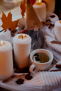 氛围灯光摄影照片_感恩节和 Hello Fall 万圣节概念在舒适的家中在窗台上庆祝秋季假期 Hygge 审美氛围秋叶侏儒、香料和蜡烛在温暖的黄色灯光下的针织白色毛衣上。