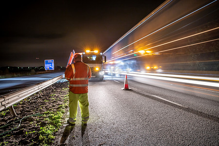 道路指示牌摄影照片_夜间高速公路上的工人与车辆驶过