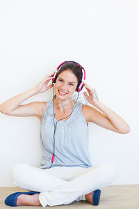 肖像、音乐和女人在工作室的地板上戴着耳机，在背景墙上快乐地流媒体。