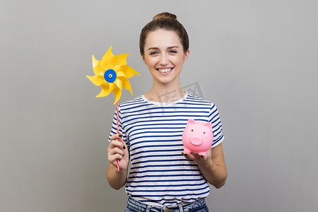 钱表情摄影照片_女人拿着折纸手磨棒和存钱罐，用快乐的表情看着相机。