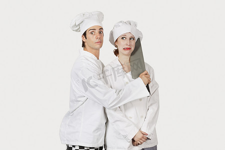 灰色背景下男厨师用切肉刀攻击女同事的画像
