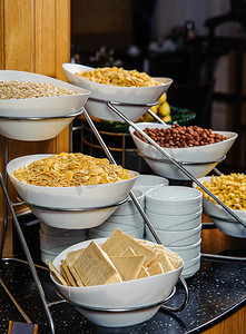 自助早餐摄影照片_一张自助餐桌的垂直照片，上面摆满了碗，早餐时放着玉米片、花生和麦片