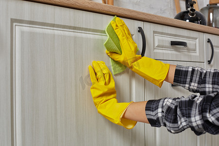 戴着绿色抹布手套的手正在清洁厨柜 — 家务和家政概念