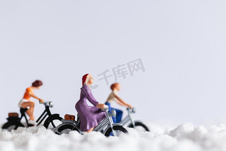 人物冷摄影照片_微型人物：在雪地背景上骑自行车的旅行者