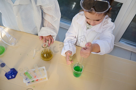 一个聪明的女学生使用带刻度的移液器的俯视图，将少量试剂滴入装有化学溶液的烧杯中