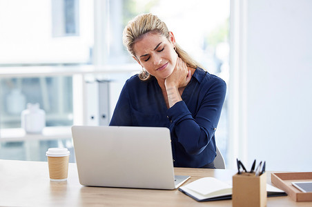 工作压力、在办公桌前颈部疼痛并在伦敦办公室的笔记本电脑上阅读电子邮件的女商人。