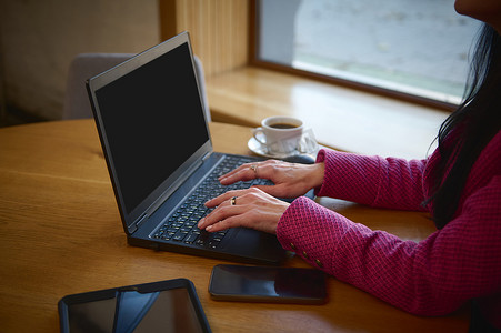 手机文案摄影照片_在远程办公时，专注于笔记本电脑键盘上的女商人的手，坐在桌边，在咖啡馆里喝杯咖啡