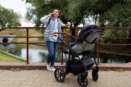 快乐的年轻女父母带着小儿子坐在婴儿车里在公园里散步
