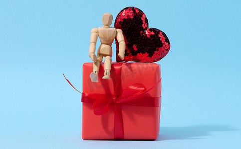 一个木制人体模型和一颗由亮片制成的红心和一个用红纸包裹的盒子，祝贺假期